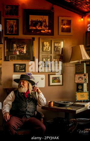 Ein reifer Mann mit Cowboyhut und Zigarre in einem schwach beleuchteten Raum Stockfoto