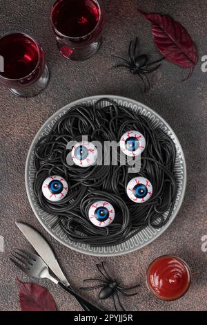 Halloween italienische schwarze Pasta dekorierte Horroraugen auf grauem Teller auf braunem Hintergrund, Draufsicht Stockfoto