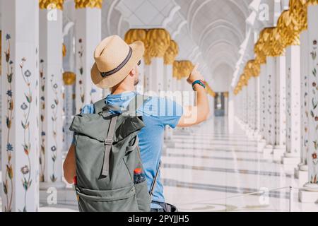 Ein Tourist mit Hut und Rucksack, der durch die große Moschee von Scheich Zayed in Abu Dhabi spaziert Stockfoto