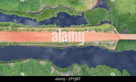 Luftaufnahme senkrecht nach unten auf der unbefestigten Straße Transpantaneira mit Auto und angrenzenden blauen Lagunen und grünen Wiesen, Feuchtgebieten, Mato Grosso, Brasilien Stockfoto