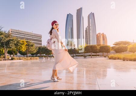 Erleben Sie die Verschmelzung von Moderne und Tradition, während eine indische Frau vor dem Hintergrund von Abu Dhabis berühmten Wolkenkratzern spaziert. Stockfoto