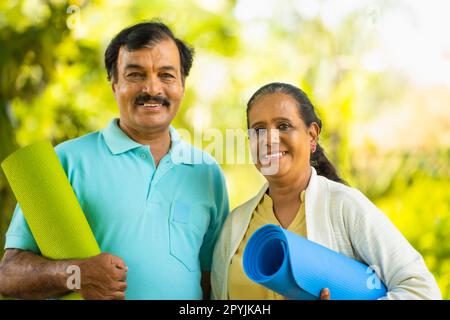 Portrait des glücklichen lächelnden indischen Seniorenpaar mit Yogamatte, die beim morgendlichen Training im Park auf die Kamera schaut - Konzept von Fitness, aktiv gesund Stockfoto