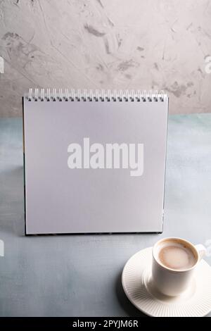Bild eines leeren Skizzenbuchs auf dem Tisch und einer weißen Tasse Kaffee Stockfoto