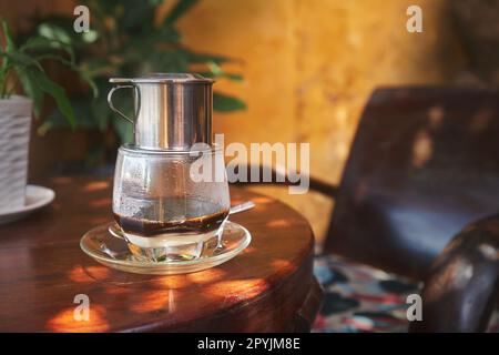 Ein Glas traditioneller heißer vietnamesischer Kaffee mit Kondensmilch auf einem Holztisch im Café in Vietnam. Stockfoto