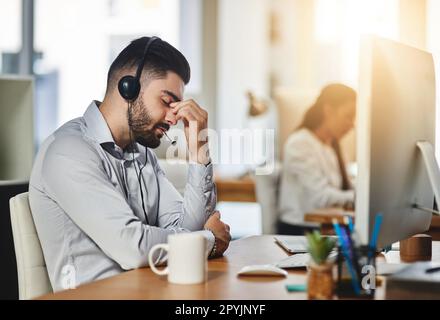 Kopfschmerzen bei der Arbeit sind nie leicht. Ein männlicher Agent hat Kopfschmerzen in einem Callcenter. Stockfoto