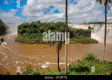 Blick auf die Isla San Martin mit braunem Fluss und Wasserfällen im Hintergrund, blauer Himmel und weiße Wolken, Iguazu Falls, Argentinien Stockfoto