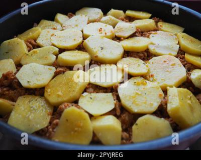 Rohe Kartoffeln, in Kreise geschnitten und auf Hackfleisch und Zwiebeln gestapelt. Moussaka-Herstellungsprozess. Gewürze auf Kartoffeln. Balkanküche: Traditionelle griechische, serbische und türkische Gerichte Stockfoto