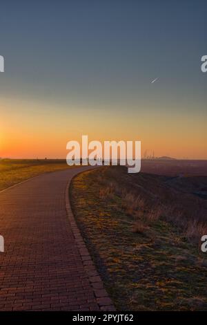 Vertikale Aufnahme eines leeren Gehwegs auf einem Hügel bei Halde Hoheward bei Sonnenuntergang in Deutschland Stockfoto