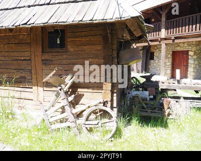 Stanisici, Bijelina, Bosnien und Herzegowina, 25. April 2021. Holzfällerhaus. Traditionelles Wohnhaus im bosnischen Gebirge aus dem 19. Jahrhundert. Restauriertes Ethno-Gebäude. Antikes Holzrad von einem Wagen Stockfoto