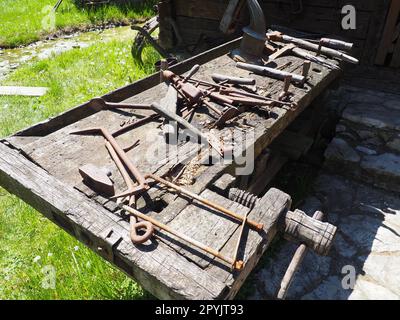 Klassische Arbeitsgeräte auf einem Holztisch. Holz- und Metallwerkzeuge für Bauwesen und Landleben. Hammer, Halterung, Säge, Axt, Bohrer, Zange, Poker, Löffel, hölzerne Schraubstock. Dorfleben. Schreinerei und Tischlerei Stockfoto