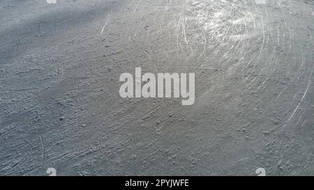 Eis gestreift mit der Spitze der Eisläufer. Eiskunstlauf. Die Oberfläche der Eislaufbahn nach dem Skater-Training. Sonnenlicht auf nassem Quelleis, Schnee und gefrorenem Wasser Stockfoto