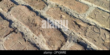 Uralter Bürgersteig. Bürgersteig aus grauen und beigen Steinen. Kopfsteinpflaster auf dem Platz der Altstadt. Unebene Fliesen in einem Kreis. Natürliche Steinstruktur Stockfoto