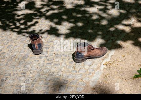 Ein Paar alte, getragene braune Laufschuhe, die auf dem Weg zurückgelassen wurden. Verlassene Schuhe sind unterwegs. Stockfoto