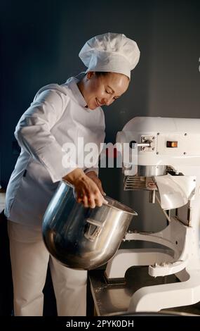 Weibliche Bäckerin in professioneller Küche mit Teigmischer in der Bäckerei Stockfoto