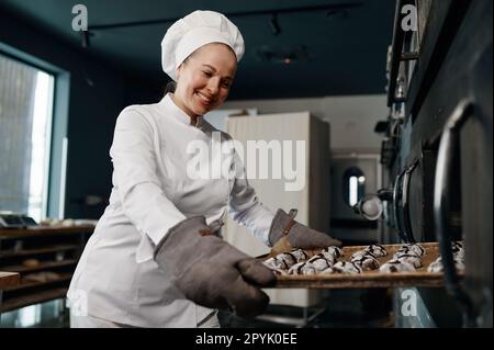 Ein fröhlicher, lächelnder Bäcker, der ein Tablett mit gekochten Haferbrei-Keksen hielt Stockfoto