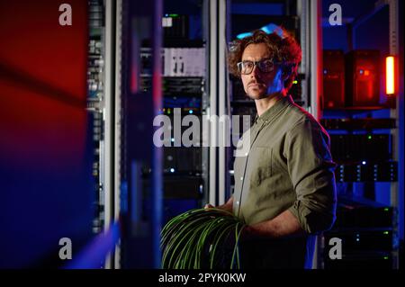 Rechenzentrumsingenieur mit vielen optischen Kabeln, die neben Computer-Racks laufen Stockfoto