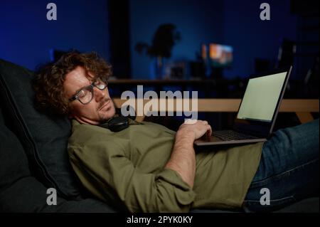 Müder Systemadministrator schläft unter einem Laptop auf dem Sofa im Serverraum Stockfoto