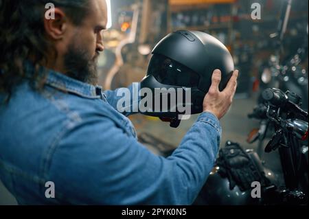 Seitenansicht des Motorradfahrers bei der Auswahl eines neuen, modernen Schutzhelms im Motorradladen Stockfoto