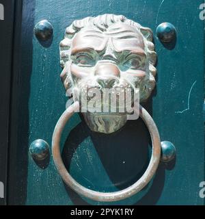 Ein Türklopfer ist eine Vorrichtung an der Haustür eines Hauses. Sie besteht aus Metall und hat die Form eines Rings, der auf den Metallteil des an der Wand befestigten Türklopfers geklopft wird. Mündung eines Löwen. Stockfoto