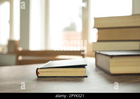 Lernkonzept für den Bildungsbereich mit einem Buch oder Lehrbuch zu Hause im Bürozimmer, Stapel von Literaturarchiv auf dem Lesetisch und Gang von Bücherregalen im Unterrichtsraum im Hintergrund Stockfoto