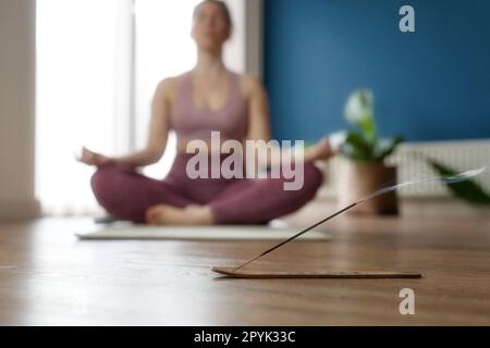 Die Hand der Frauen in Lotus posiert, während sie zu Hause im Morgensonnenlicht am Boden sitzen. Dolly-Shot, Konzept der Entspannung und Meditation mit Weihrauch im Wohnzimmer Stockfoto