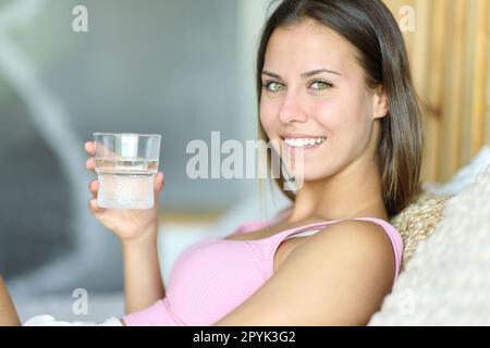 Ein Teenager mit einem Glas Wasser schaut in die Kamera im Bett Stockfoto