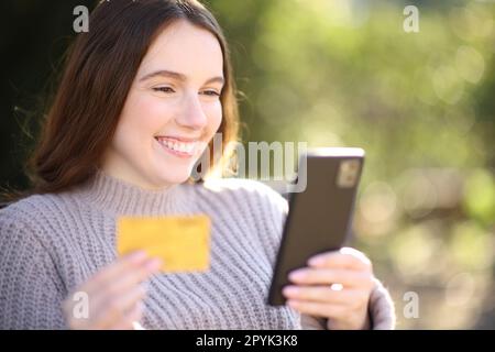 Glückliche Frau, die online in einem Park einkauft Stockfoto