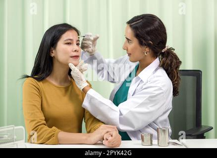 Arzt in weißem Kleid und Schutzhandschuh gibt der Patientin eine medizinische Injektion in die Stirn. Stockfoto