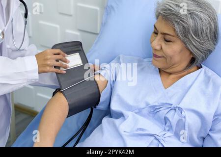 Ältere Patientin und Ärztin. Der junge Arzt misst den Druck eines älteren Patienten im Aufwachraum. Gesundheits- und Medizinkonzept. Stockfoto