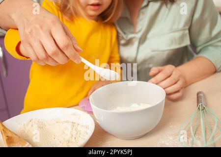 Großmutter und Enkelin bereiten Kuchenteig zu, verbringen Zeit miteinander, Familienbeziehungen, Liebe. Gieße Zucker in eine Tasse. Stockfoto