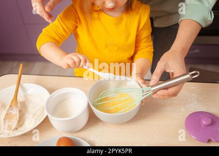 Großmutter und Enkelin bereiten Kuchenteig zu, verbringen Zeit miteinander, Familienbeziehungen, Liebe. Löffel mit Zucker. Stockfoto