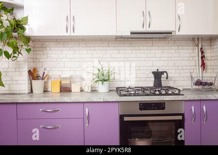 Küche lila, lavendelfarben, weiße Schränke, grüne Blumen, schwarzer Ofen. Hintergrund. Stockfoto