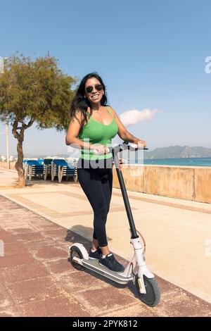 Eine Frau, die mit einem elektrischen Roller fährt, eine glückliche Sommerfahrt im tropischen Insel-Strandresort für den Urlaub. Stadt, Straße und umweltfreundliche Verkehrsmittel, Spaß auf escooter im Urlaub auf mallorca, balearische Insel Stockfoto