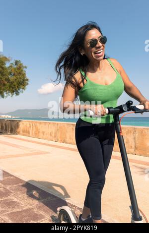 Eine Frau, die mit einem elektrischen Roller fährt, eine glückliche Sommerfahrt im tropischen Insel-Strandresort für den Urlaub. Stadt, Straße und umweltfreundliche Verkehrsmittel, Spaß auf escooter im Urlaub auf mallorca, balearische Insel Stockfoto
