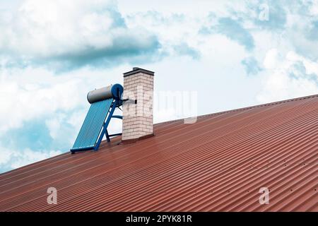 Neben dem Kamin auf einem roten Dach installierter Solar-Wasserkocher Stockfoto