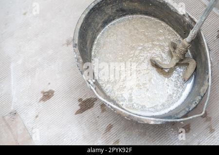 Manuelles Mischen von Zement mit Hilfe eines elektrischen Mischers, Zement in einem Eimer auf einer Baustelle Stockfoto