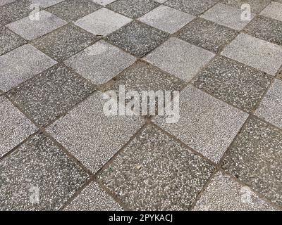 Schachfliesen. Einfarbige Asphaltmarkierungen auf dem Sportplatz. Steinfliesen mit dunkler und heller Oberfläche. Diagonal fotografierte Quadrate oder Rhombusse. Raue felsige Oberfläche. Stockfoto