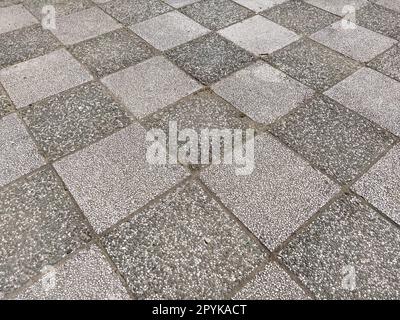 Schachfliesen. Einfarbige Asphaltmarkierungen auf dem Sportplatz. Steinfliesen mit dunkler und heller Oberfläche. Diagonal fotografierte Quadrate oder Rhombusse. Raue felsige Oberfläche Stockfoto