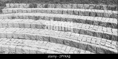 Halbschritte des Amphitheaters. Breite Treppe aus Steinblöcken oder Ziegeln. Unebene Ziegel. Die alten Stufen sind kreisförmig. Schwarzweiß-Fotografie Stockfoto