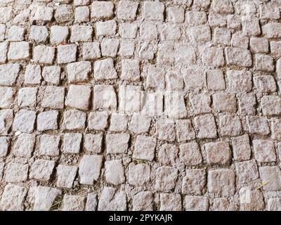 Mit unebenen Natursteinen gepflasterter Bürgersteig. Zwischen zerdrückten Kopfsteinpflaster gibt es kleine Kiesel, Erde, Sand, Gras. Platz in der alten europäischen Stadt. Stockfoto