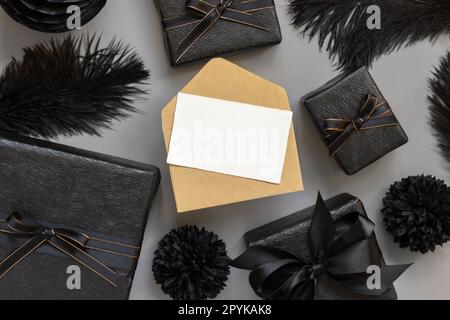 Leere Karte und Umschlag zwischen Geschenkschachteln und schwarzen Federn, Modell Stockfoto