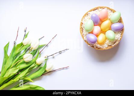 Farbenfrohe Ostereier in einem Korb. Strauß weißer Tulpen und Weidenzweige. Hintergrund. Stockfoto