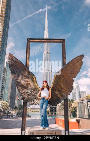 18. Januar 2023, Dubai, Vereinigte Arabische Emirate: Touristin posiert an der Statue „Wings of Mexico“ vor dem malerischen Burj Khalifa und anderen Wolkenkratzern Stockfoto