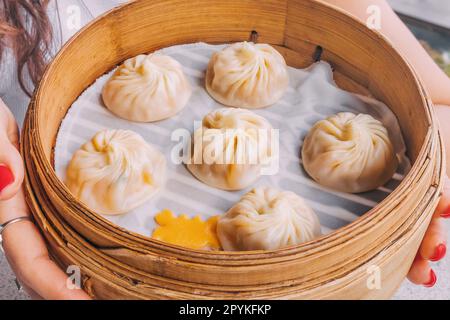 Eine köstliche, traditionelle chinesische Delikatesse, Xiao Long Bao Teigtaschen, präsentiert auf einem Bambus-Teller für einen authentischen Touch. Stockfoto