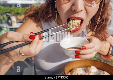 Ein Mädchen mit Stäbchen, das köstliche, traditionelle chinesische Köstlichkeiten isst, Xiao Long bao Knödel oder Baozi-Brötchen mit Sojasauce Stockfoto