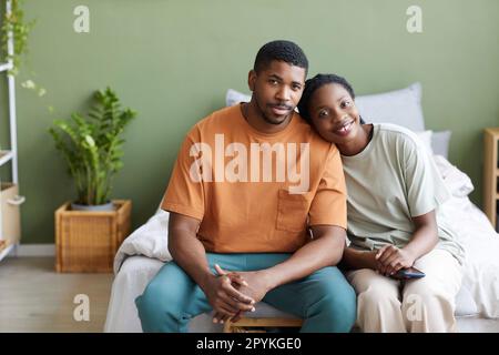 Porträt eines liebevollen afroamerikanischen Paares, das vor der Kamera lächelt, während es zu Hause im Bett sitzt Stockfoto