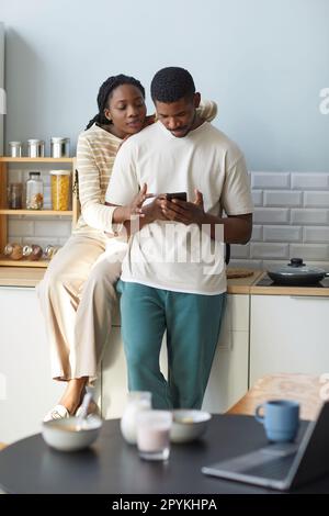 Ein afroamerikanisches junges Paar, das ein Smartphone benutzt und in der Küche steht Stockfoto