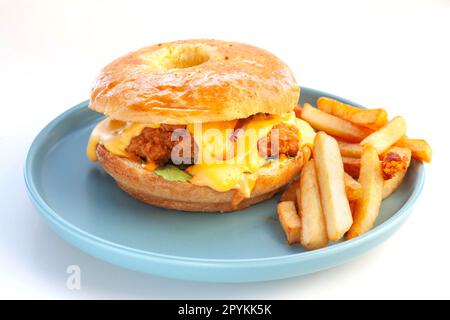 Gebratener Hähnchenburger mit Brioche Donut Brötchen und Pommes Frites auf einem blauen Teller. Stockfoto