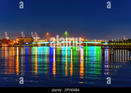 Die Queensway Bridge in Long Beach, Kalifornien, strahlt nachts hell und reflektiert das Wasser. Stockfoto