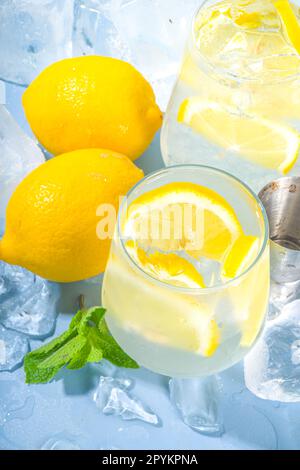 Traditionelle sommerlich kalte, erfrischende Cocktail-Limonade mit Zitronenscheiben und viel zerkleinertem Eis und vereisten Podesten auf blauem Hintergrund Stockfoto